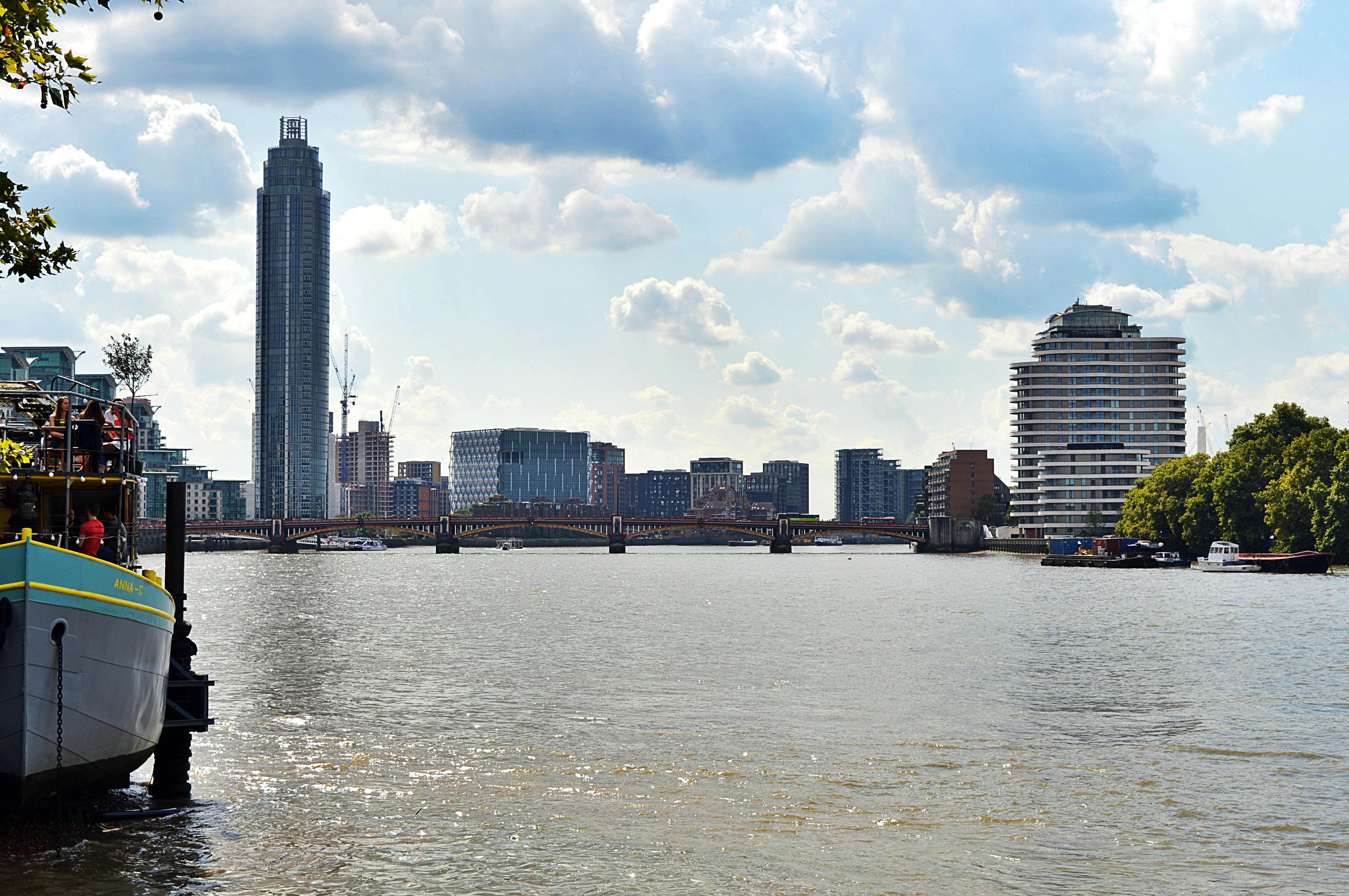 Scenic view of London's skyline featuring skyscrapers and the River Thames under a cloudy sky.