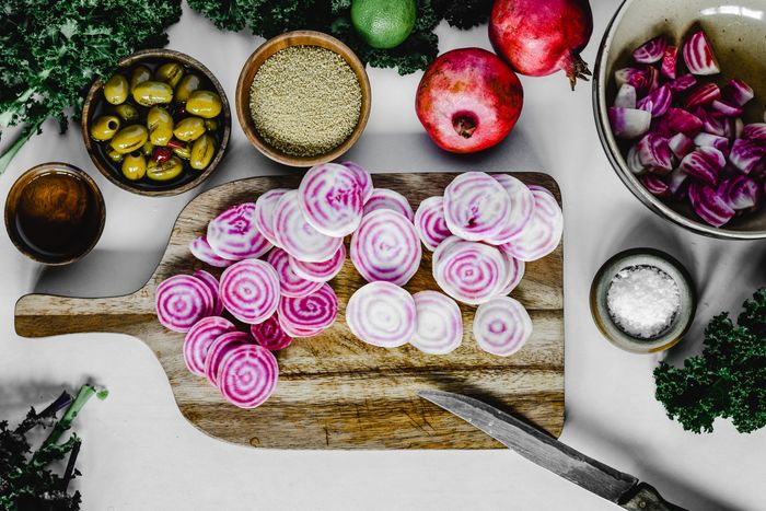 Sliced candy stripe beets on a wooden board beside olives, pomegranates, quinoa and sea salt