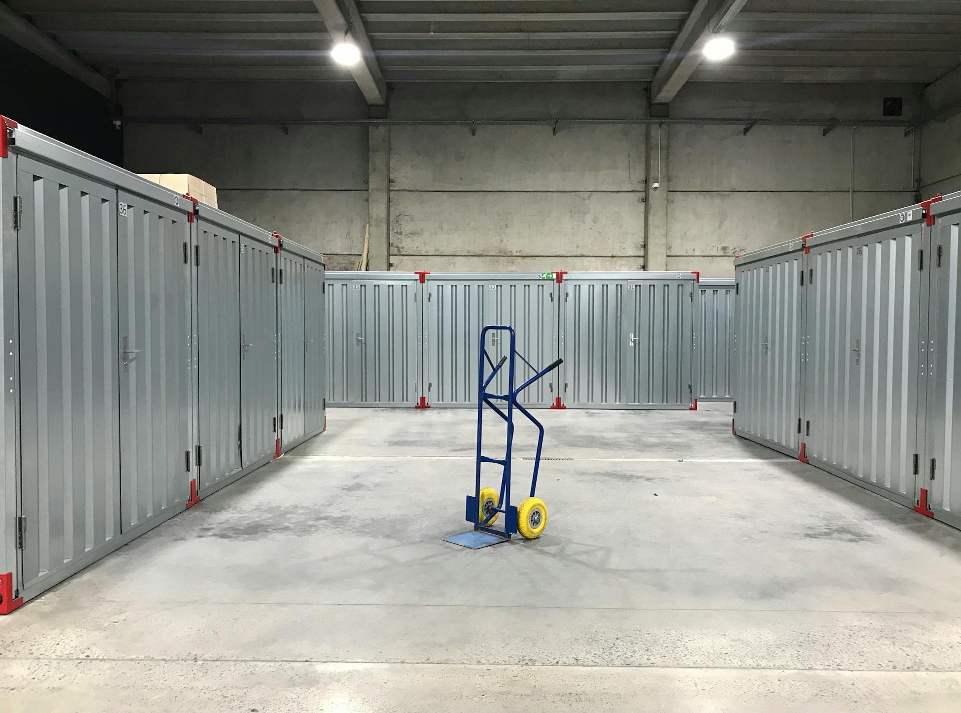 Steel storage units in an industrial warehouse with a blue hand truck in the center, ideal for logistics.