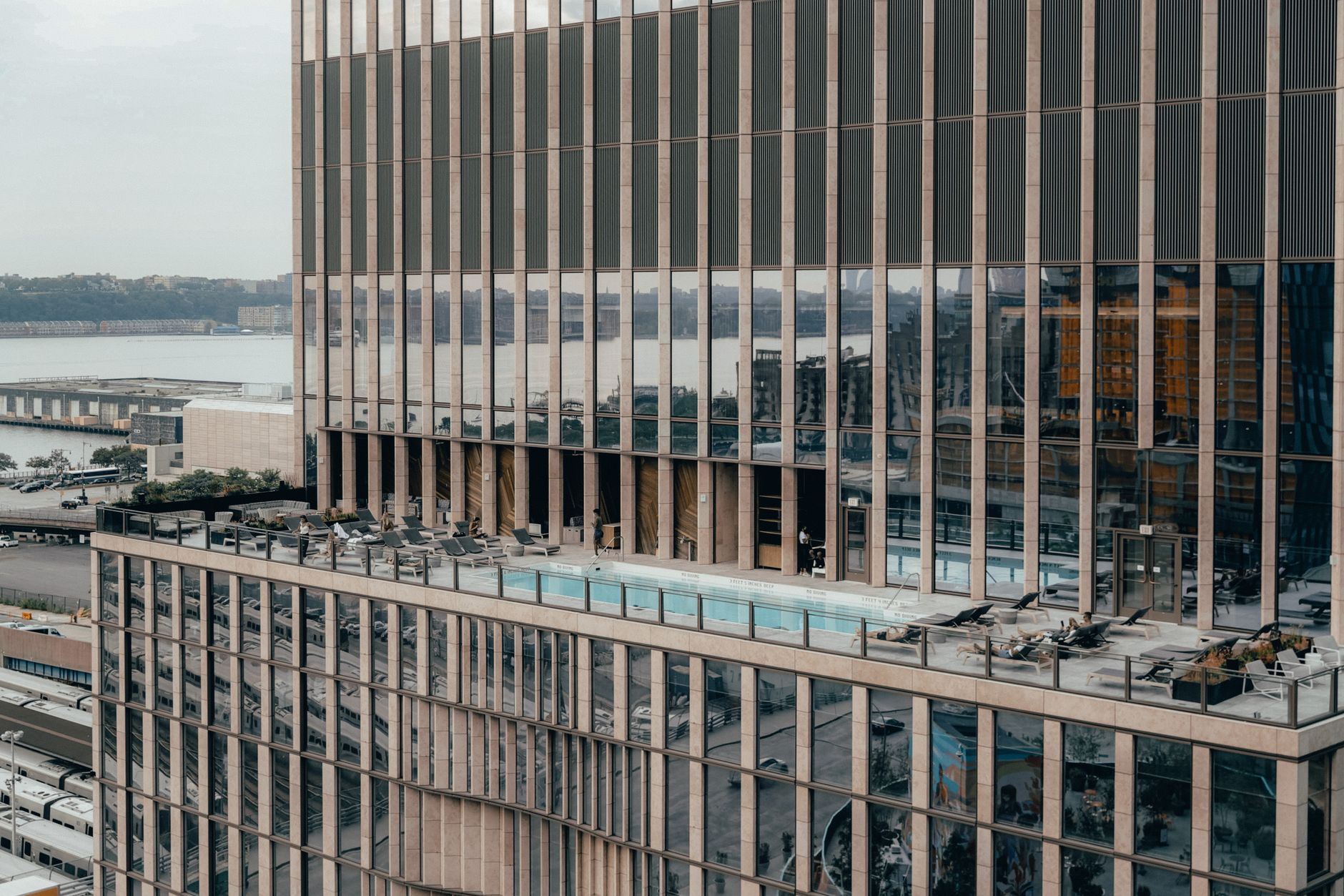 Exterior of contemporary multistage house with reflective glass walls and swimming pool with lounges on roof located on street in city