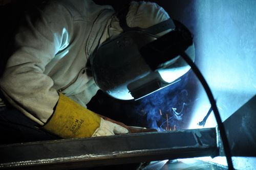 Free A welder working indoors, creating sparks, wearing safety gear in an industrial setting. Stock Photo