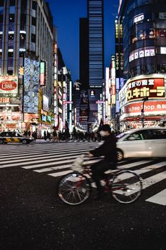 东京新宿的夜生活热闹非凡，繁忙的人行横道上，骑自行车的人穿行而过，商店灯火通明