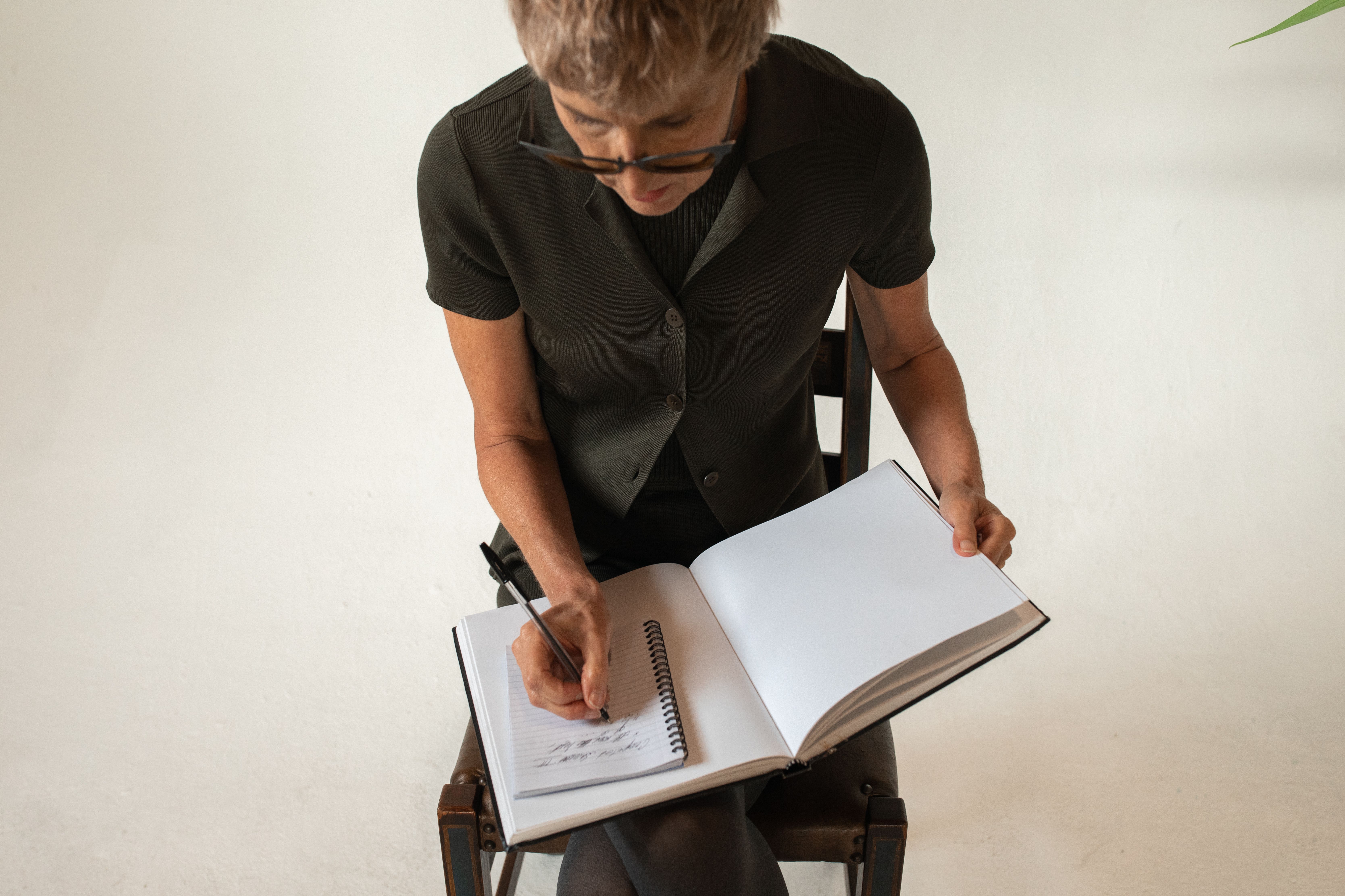 Senior adult woman writing in a notebook indoors, focusing on learning and education.