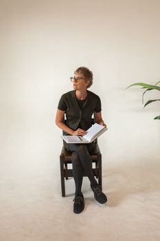 一位年长的妇女在极简主义风格的室内，于记事本上写作