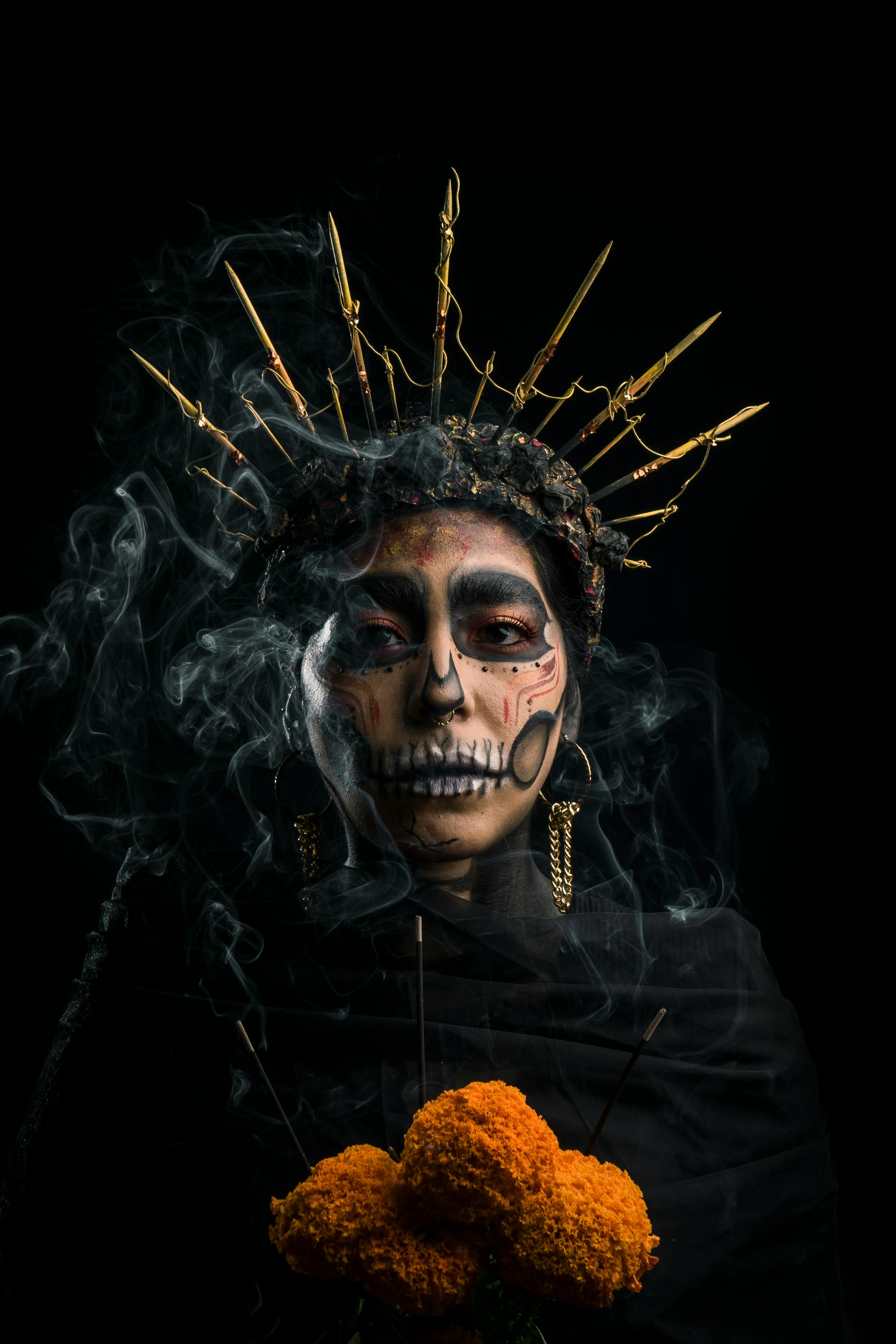 Stunning portrait of a woman in Día de los Muertos skull makeup with a crown and marigold flowers.