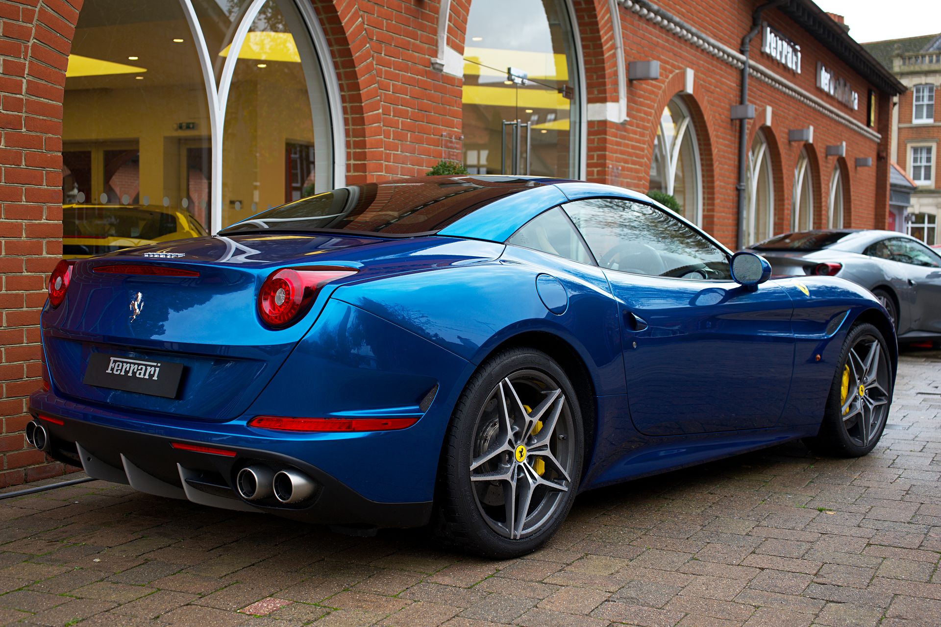 Sleek blue Ferrari sports car parked outside a dealership in the UK, showcasing luxury design.