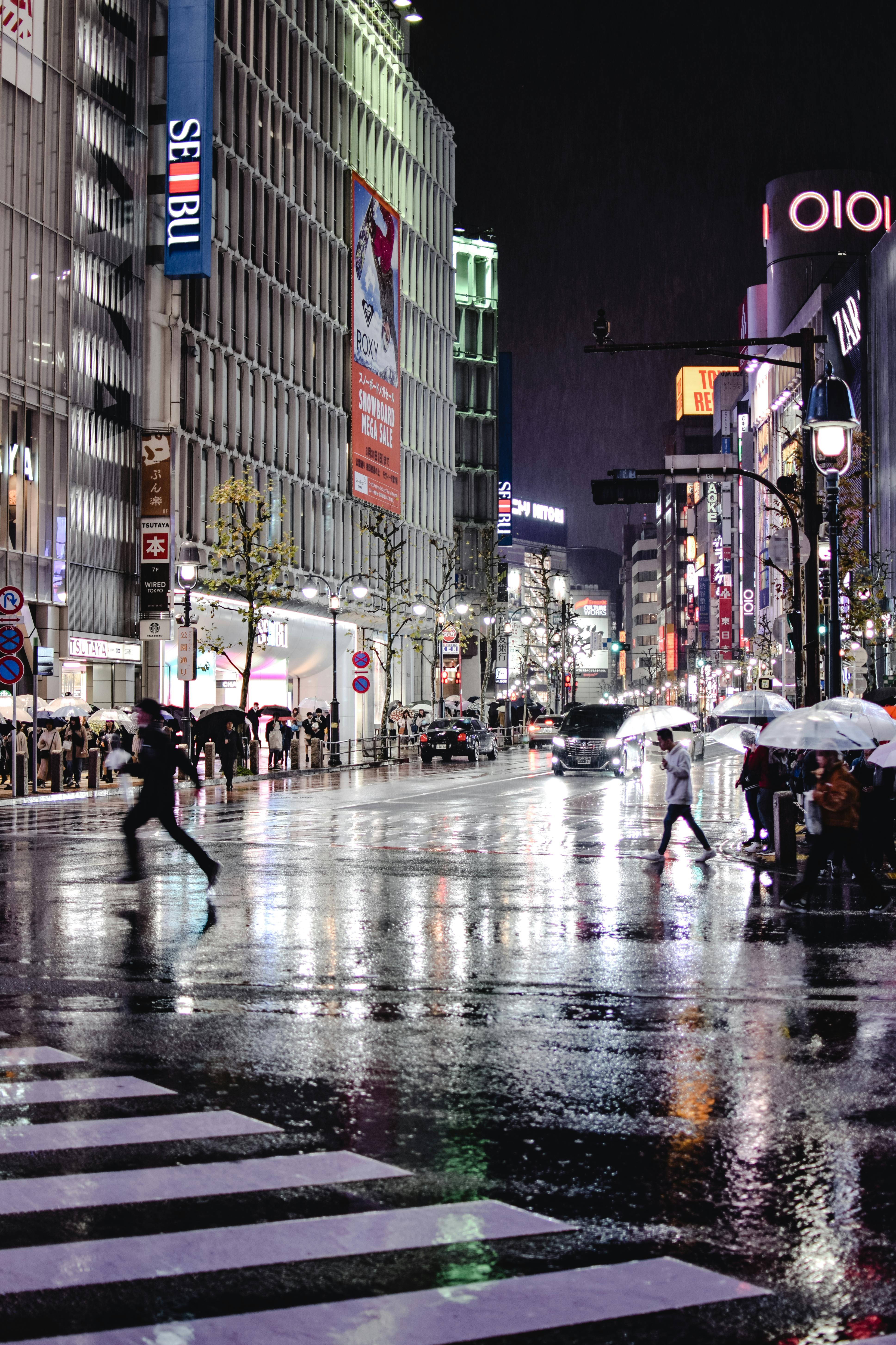 雨夜的东京涉谷路口，潮湿的道路映出倒影，行人撑着伞