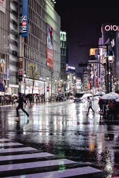 雨夜的东京涉谷路口，潮湿的道路映出倒影，行人撑着伞