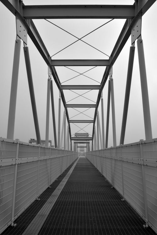 Free Grayscale image of a narrow steel pedestrian bridge in Pontocello, Veneto, showcasing geometric patterns. Stock Photo