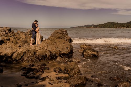 Free A couple shares an intimate embrace on a scenic rocky beach with waves in the background. Stock Photo