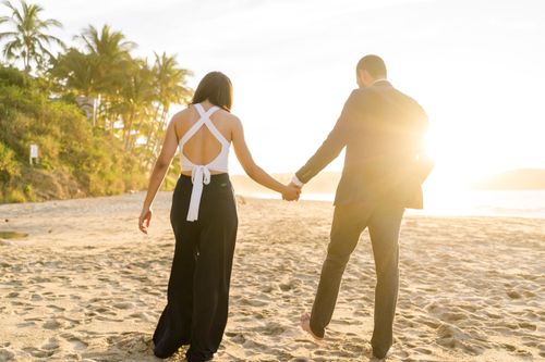 Free A romantic couple holding hands while walking on a sunny beach at sunset. Stock Photo