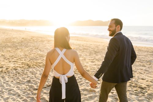 Free Happy couple holding hands and walking on a sandy beach at sunset. Stock Photo