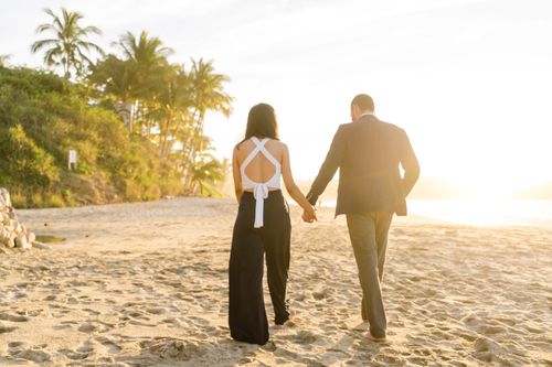 Free A couple holding hands, walking on a sandy beach during a golden sunset. Stock Photo