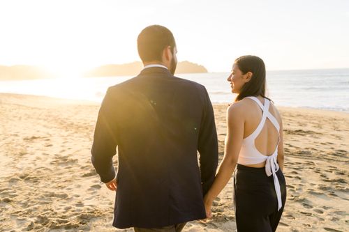 Free A couple walks hand in hand on a sunlit beach, capturing a romantic sunset moment. Stock Photo