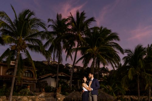 Free Couple enjoying a romantic moment under palm trees during a vibrant sunset inspiring love and tranquility. Stock Photo