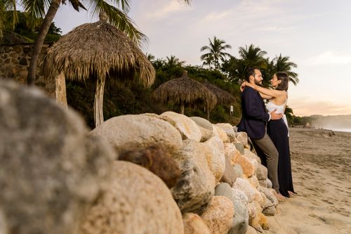Free Couple embracing by palm trees and huts on a serene tropical beach at sunset. Stock Photo
