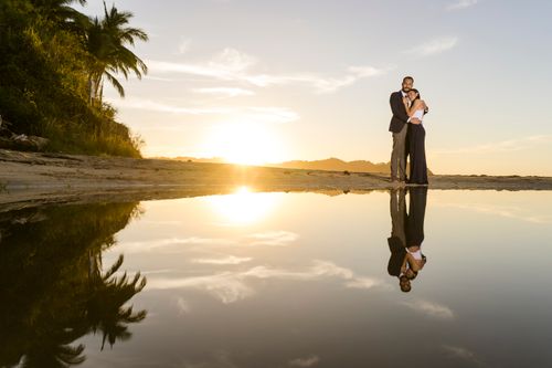 Free A couple embracing on a beach at sunset with a stunning water reflection. Stock Photo
