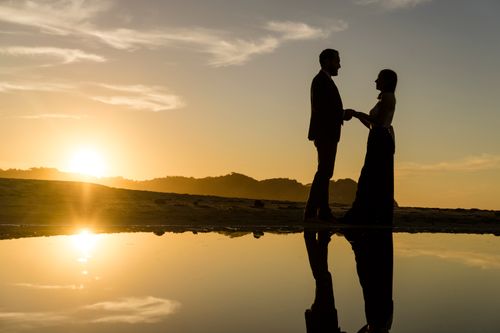 Free Silhouetted couple on the beach at sunset, reflecting on water. Romantic and serene atmosphere. Stock Photo