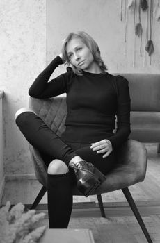 Black and white of contemplative young female leaning head on hand and looking away thoughtfully while spending time alone at home