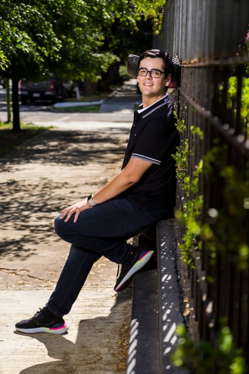 Free Casually dressed young man smiling while sitting outdoors by a fence. Stock Photo
