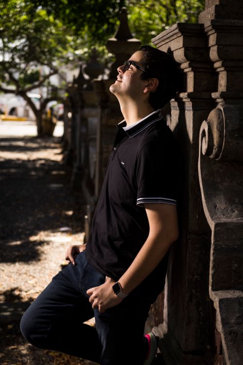 Free A man in a polo shirt enjoys a sunny day outdoors, leaning against a stone wall. Stock Photo