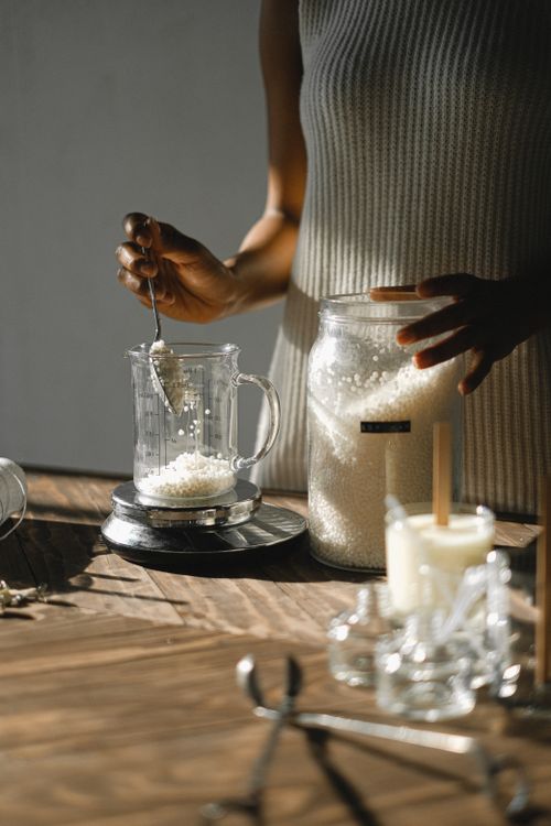 Free Unrecognizable African American female pouring wax flakes into glass jug put on scales standing at wooden table during candle making in studio Stock Photo