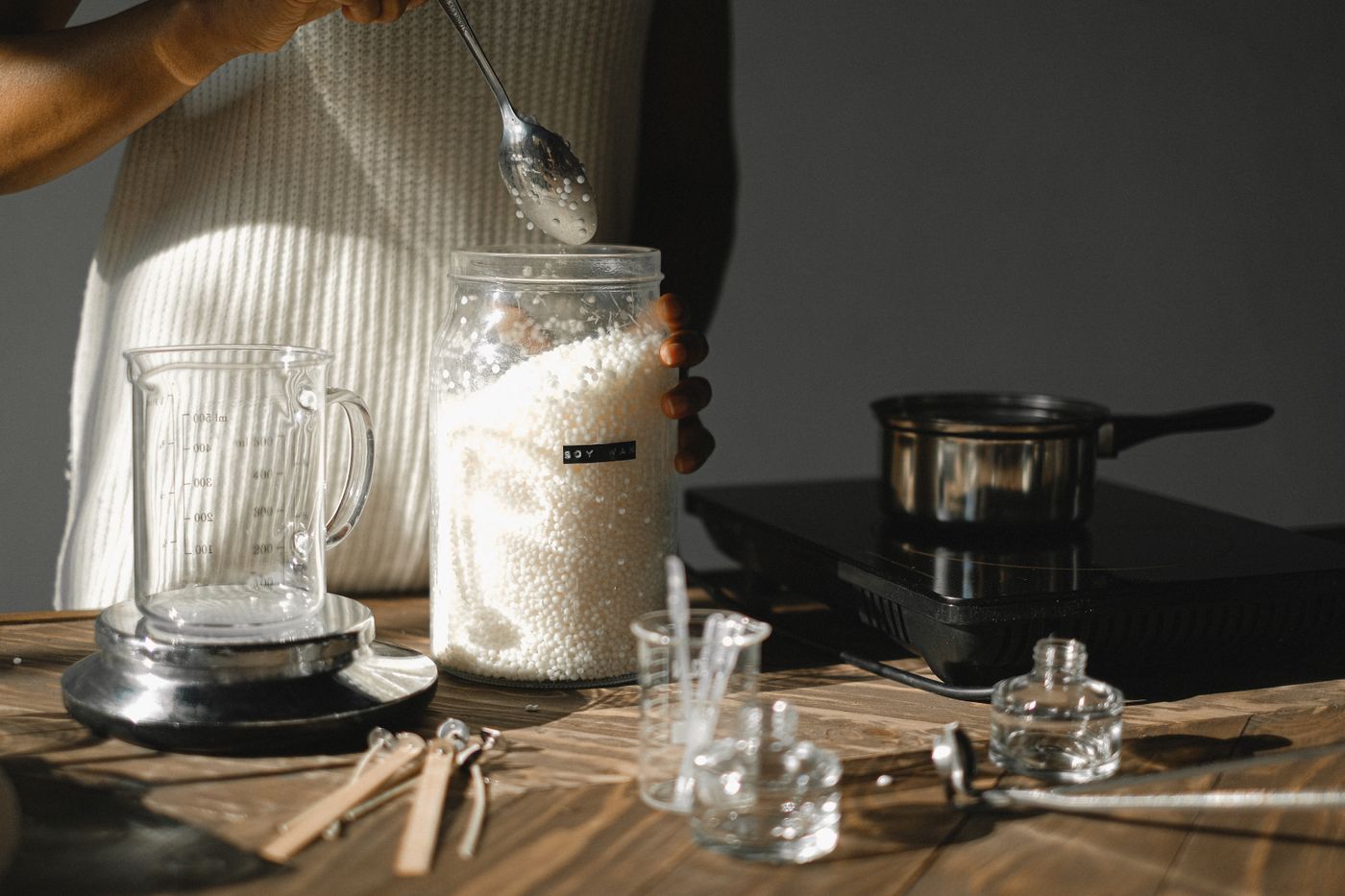 A person measuring white wax pellets at a candle-making workbench.