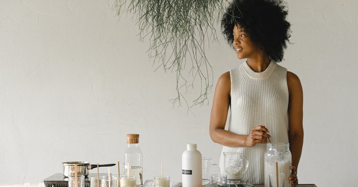 Content African American female artisan with jar of wax flakes looking away while creating candles in modern workshop in light room