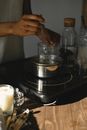 Anonymous African American female melting wax in metal pot at wooden table with cooker while making candle in light room