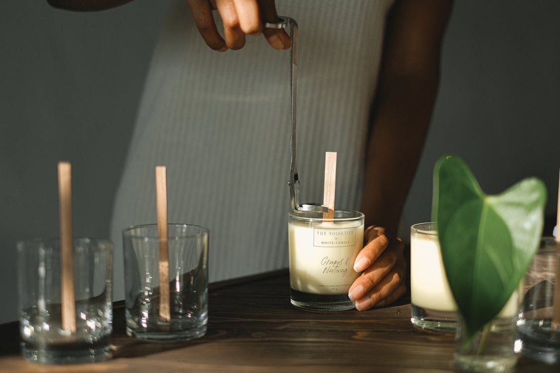 Crop black woman with trimmer preparing candles with wicks