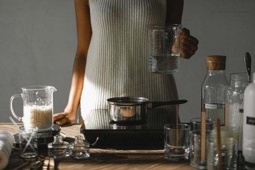 Crop black woman with melted wax at stove making candles