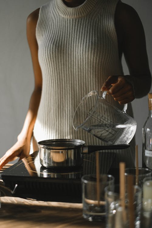 Crop black woman at stove with water