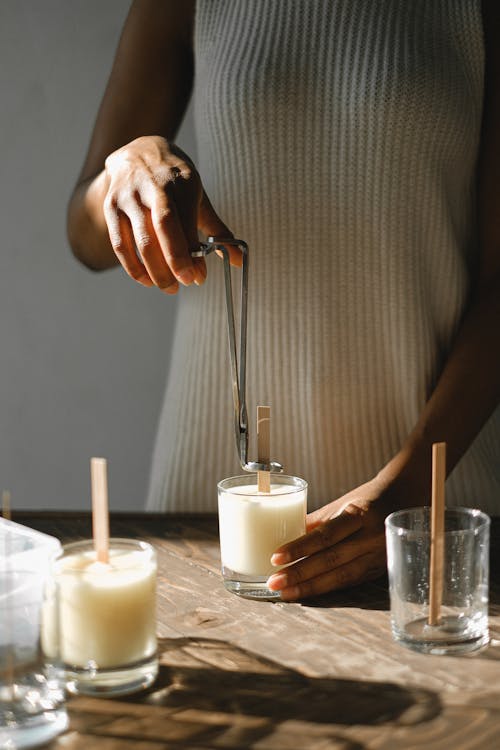 Unrecognizable African American female standing at wooden table with candle and steel wick dipper in light room with sunlight