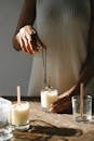 Unrecognizable African American female standing at wooden table with candle and steel wick dipper in light room with sunlight