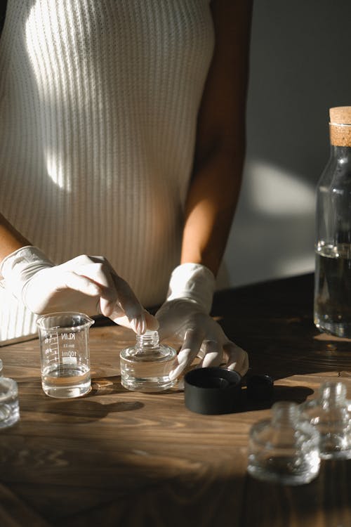 Free Crop faceless black female standing at table with glass bottles and preparing liquid incense using essential oils Stock Photo