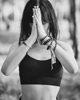 Black and white of concentrated lady in sports bra meditating with prayer hands in nature