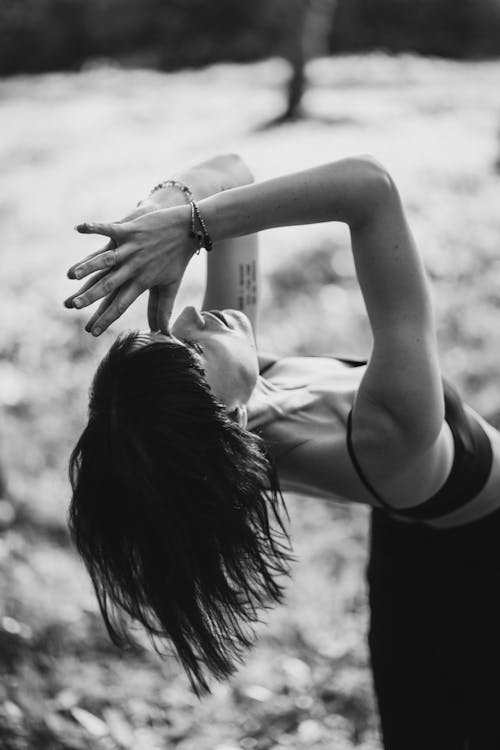 Black and white of concentrated woman with tattoos doing Camel pose with namaste in countryside