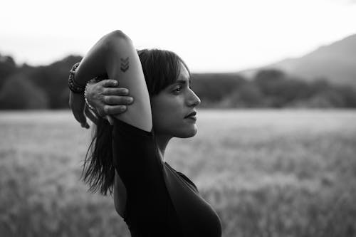 Black and white side view of thoughtful woman with tattoo looking away in meadow