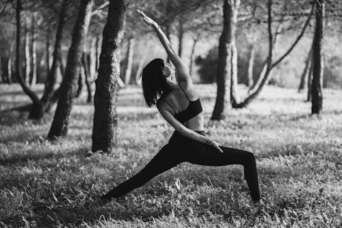 Black and white of anonymous barefoot woman in sportswear doing yoga asana in park in daylight