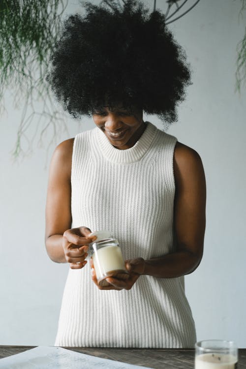 Free Positive African American female artisan standing at table with handmade candles in glasses in workshop Stock Photo