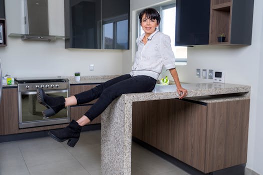 A woman casually sits on a modern kitchen counter in a brightly lit space, exuding elegance and comfort.