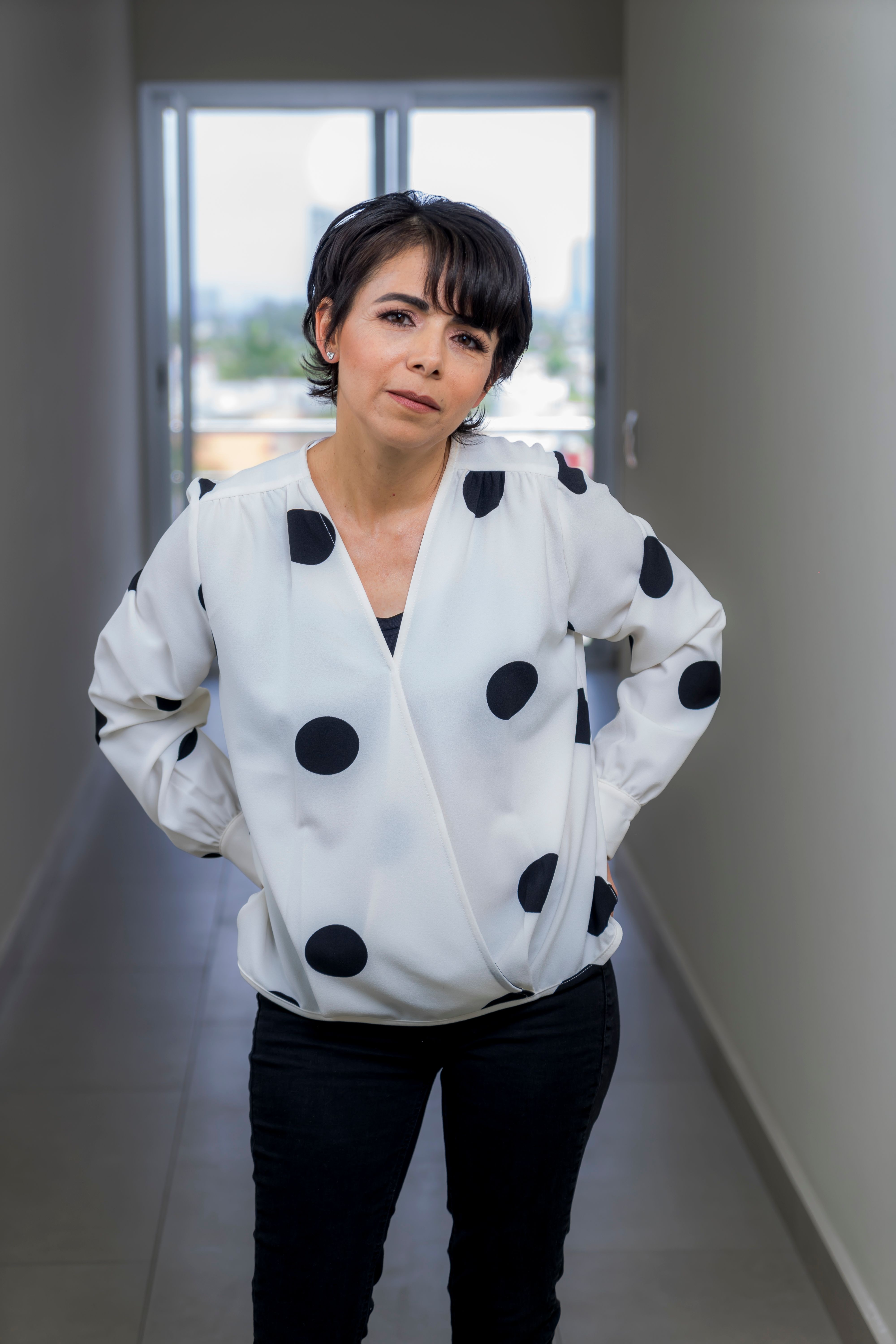 Portrait of a woman in a polka dot blouse standing indoors with a confident expression.