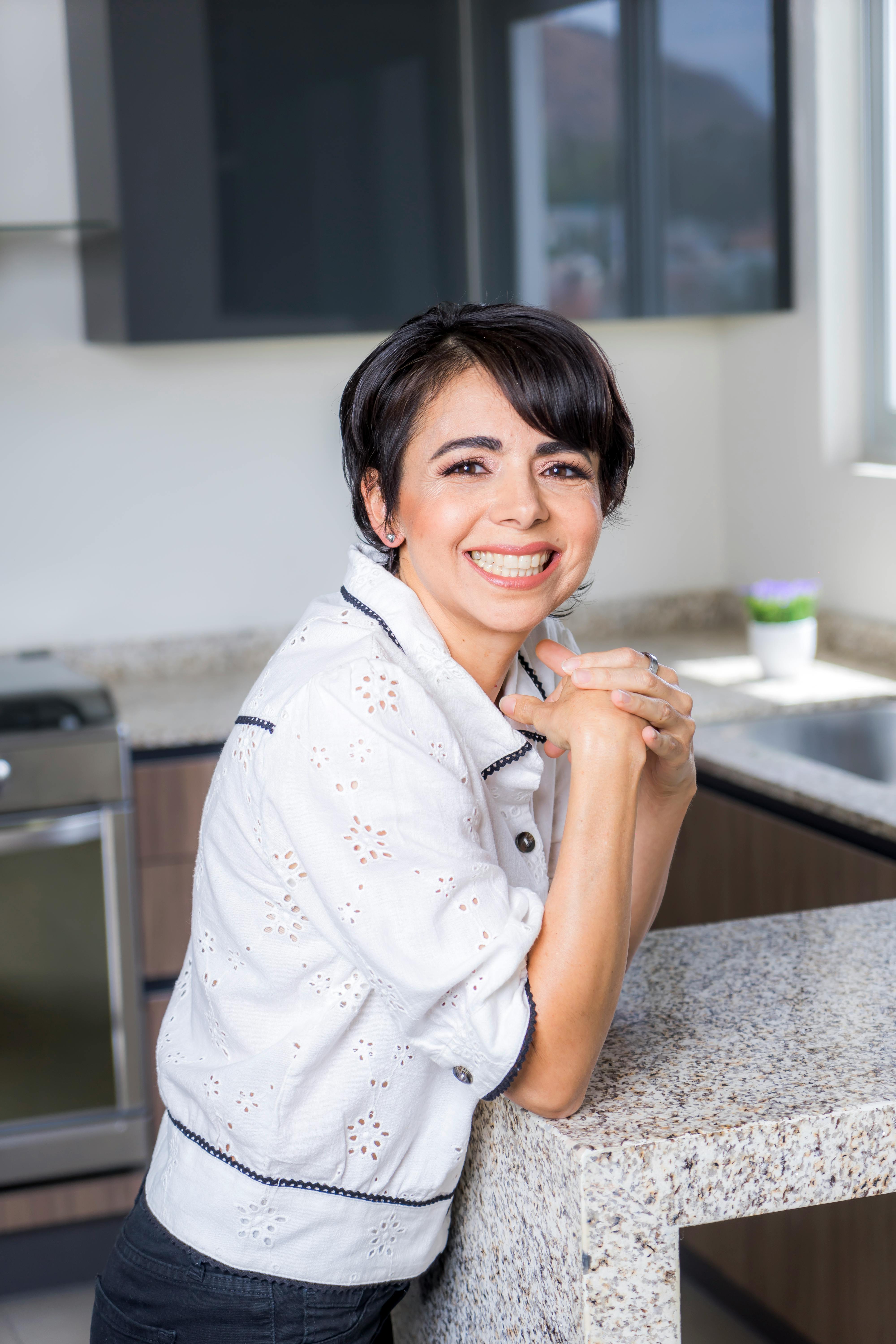 Cheerful woman in a modern kitchen leaning on a granite countertop, smiling at the camera.
