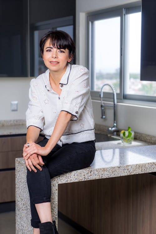 Free A Smiling Woman Sitting on the Kitchen Counter Stock Photo