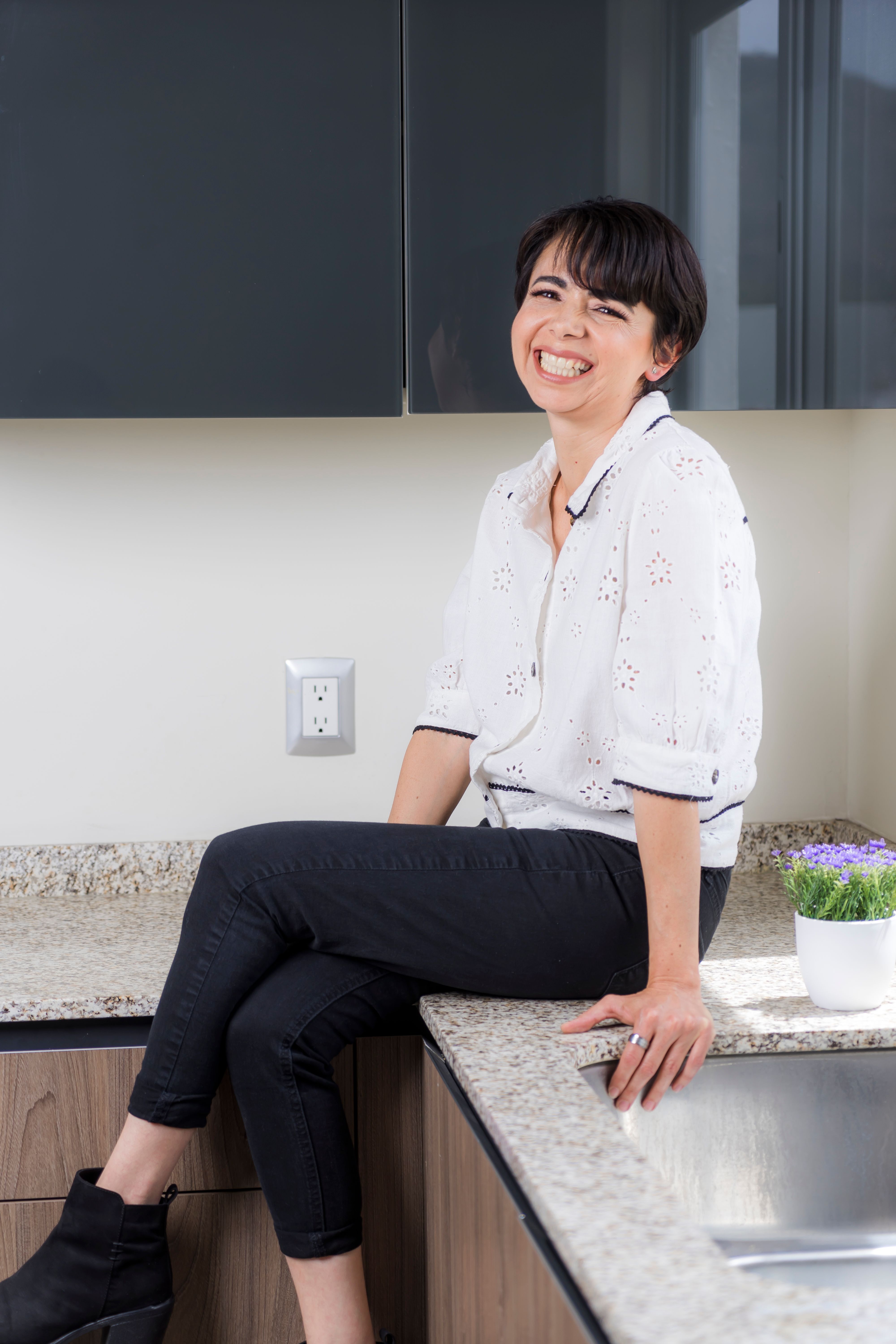 Happy woman sitting on a kitchen counter in a bright modern kitchen.