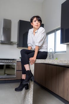 Modern kitchen scene with a stylish woman in black and white attire sitting on a countertop.
