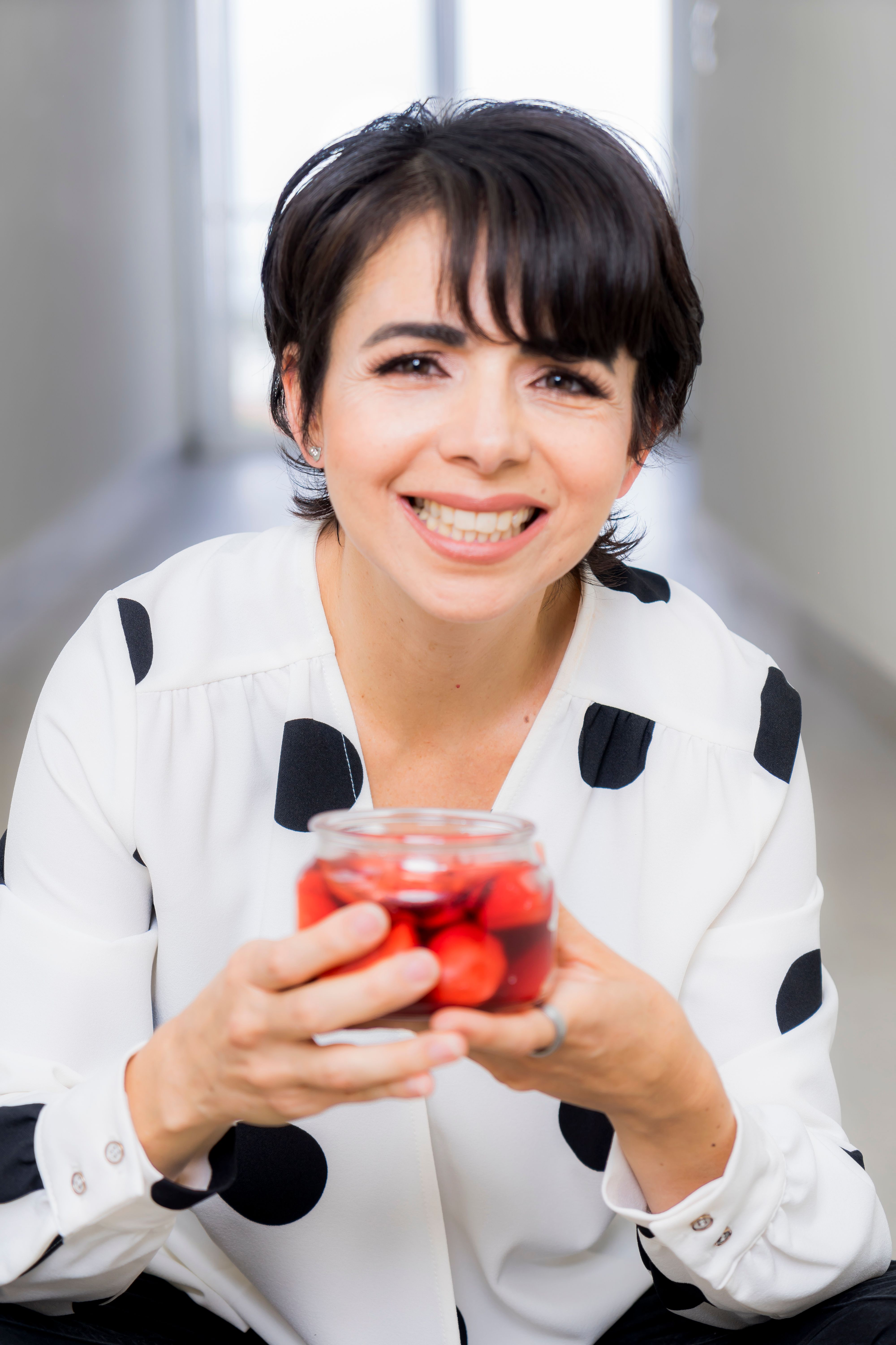 Cheerful woman holding a jar of berries in a bright indoor setting.