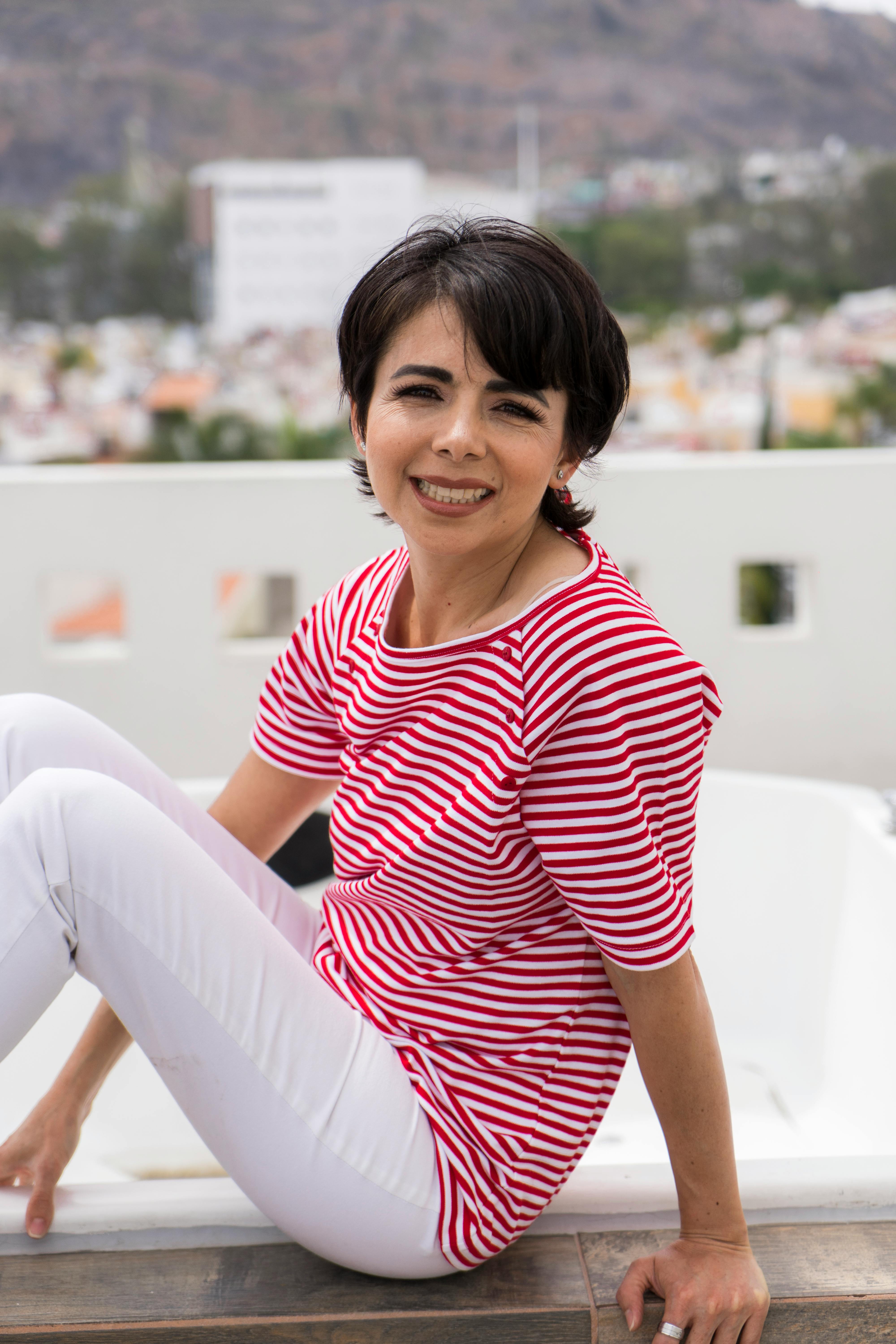 Happy woman in a red striped shirt sits outside, enjoying a relaxing day.