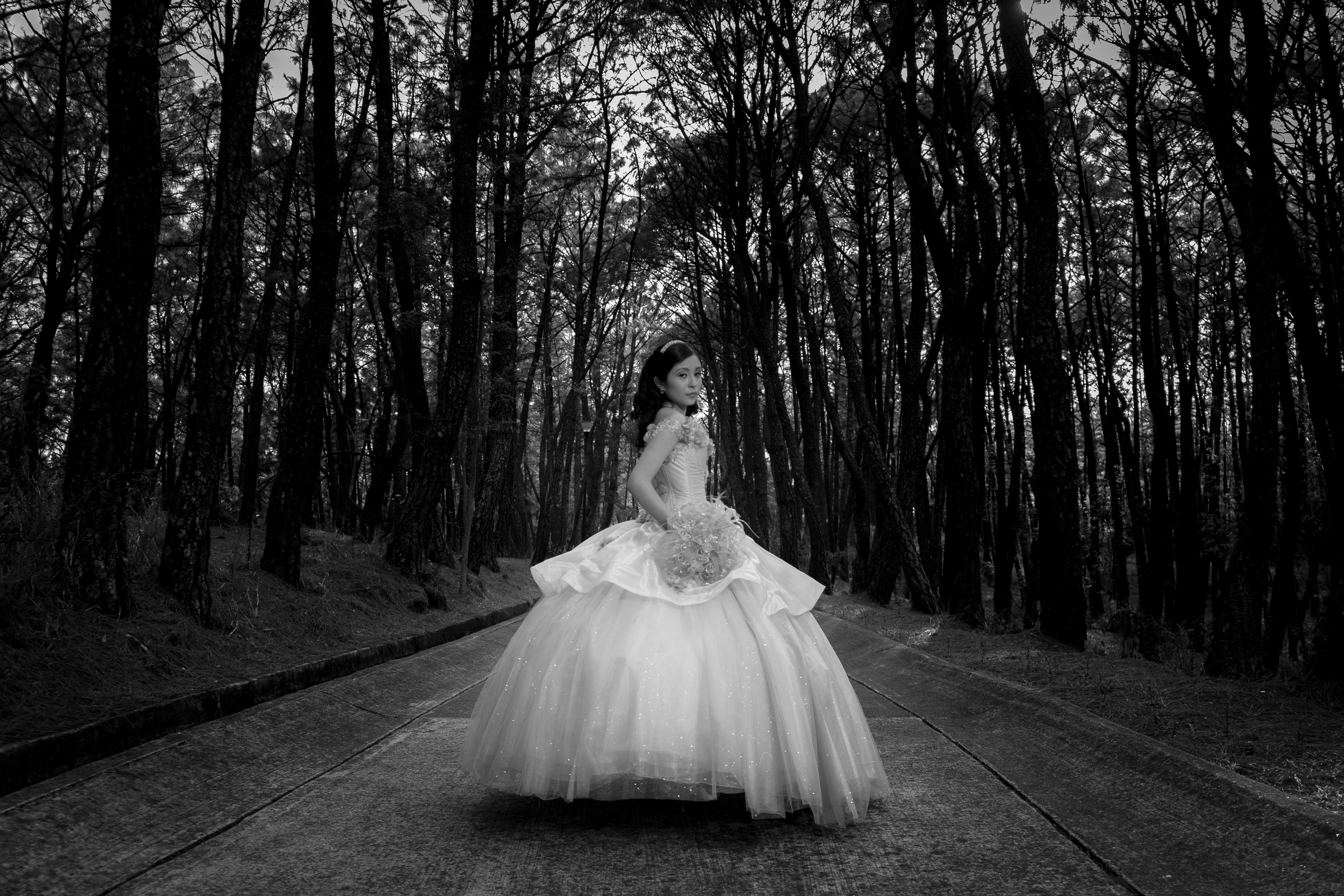 Elegant bride in white dress posing on a forest road, embodying timeless fashion.