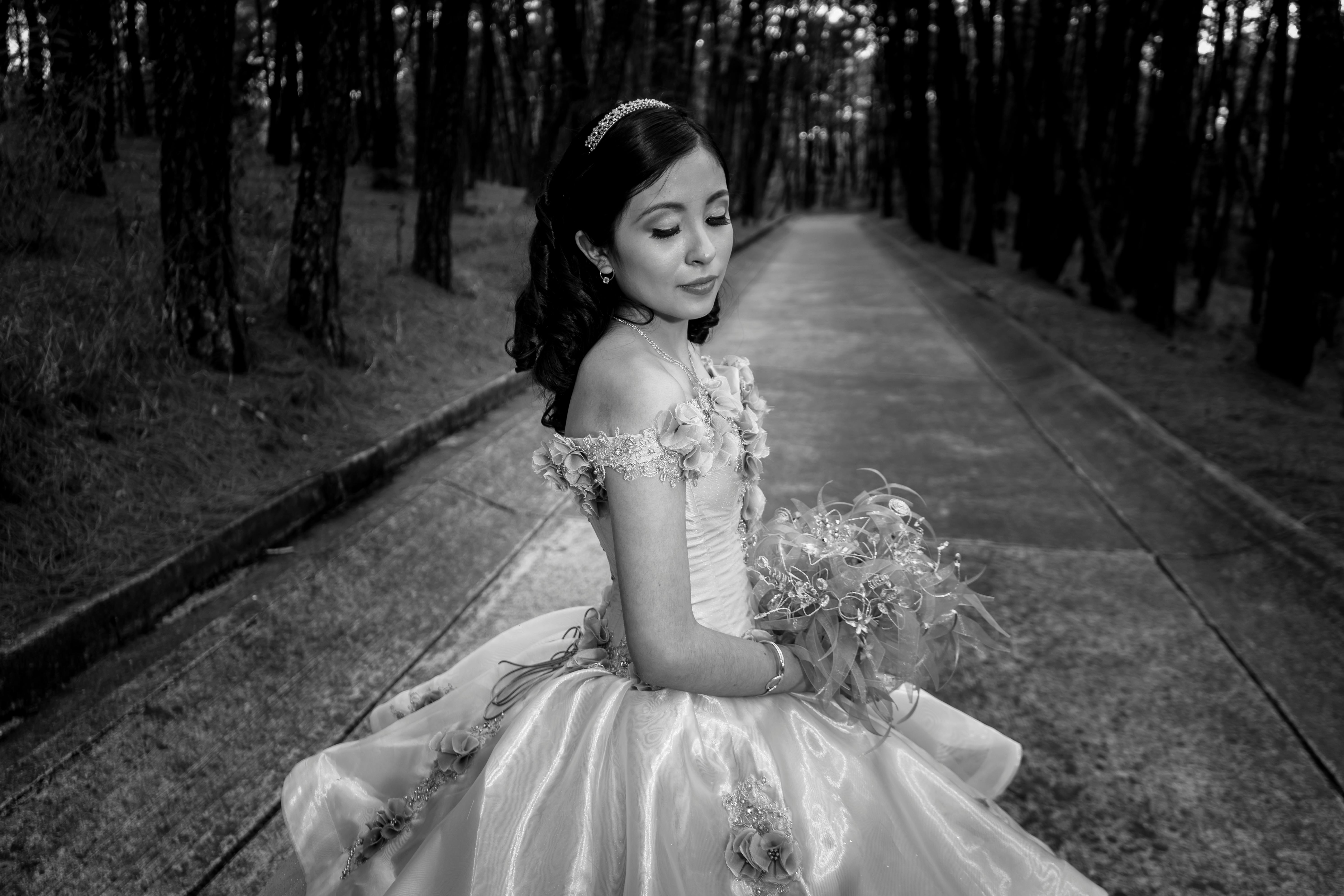 A young woman in a ball gown poses elegantly on a forest path in monochrome. | BocaVibe